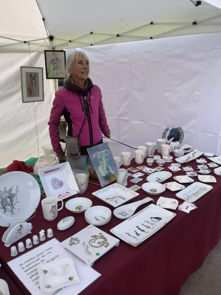 Un stand de peintures et de porcelaines décorées de lévriers. Artiste sous tente du village des exposants.