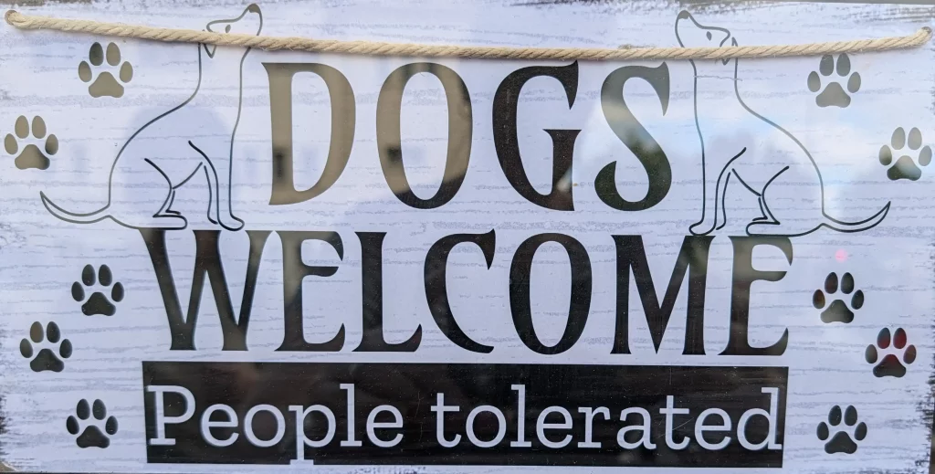 Panneau "Dogs Welcome/People tolerated" indiquant que les chiens sont acceptés et les gens tolérés dans ce lieu.